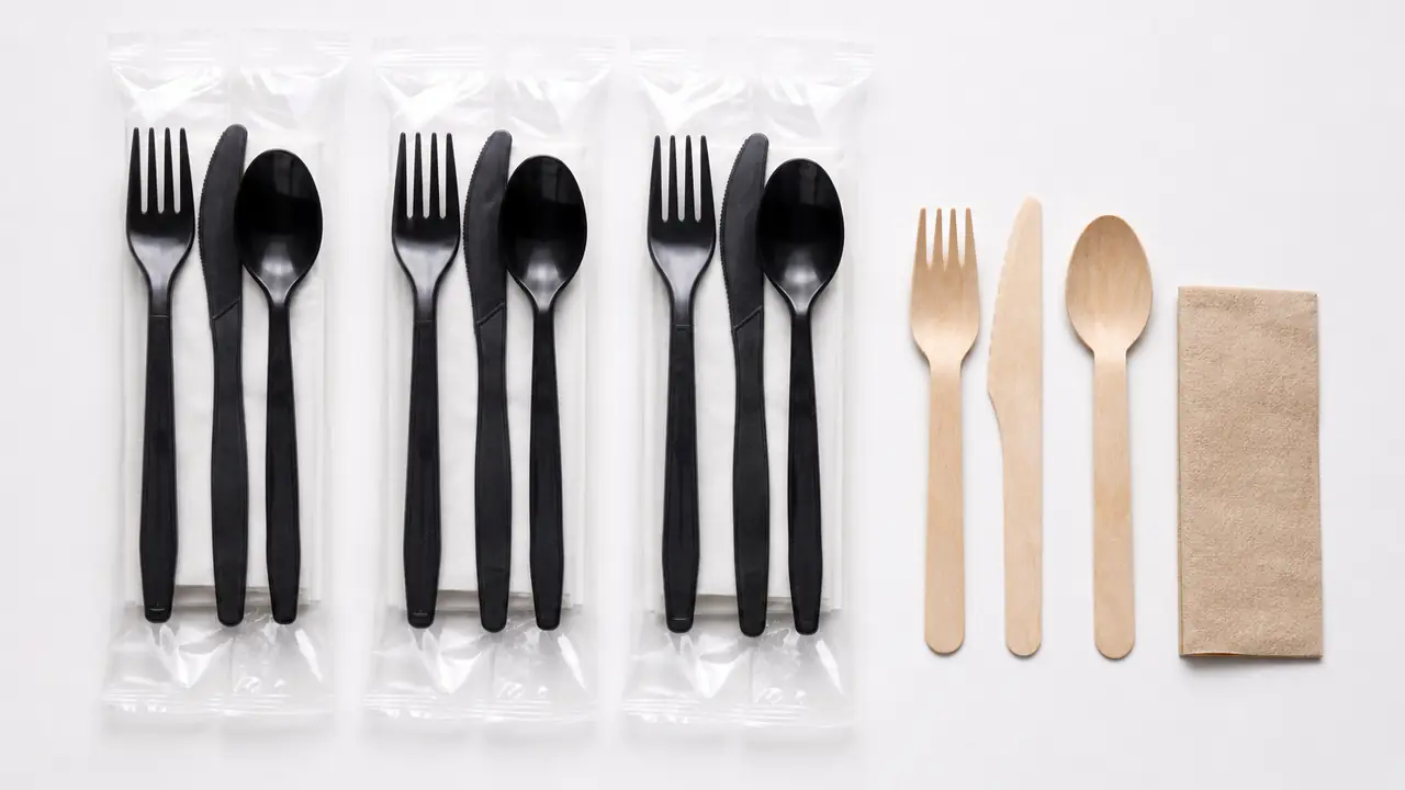 Disposable cutlery sets with PP spoons, a napkin and a toothpick in clear OPP wraps on a kraft paper bench